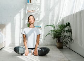 beautiful happy girl with closed eyes practicing yoga in lotus position in bedroom in the morning