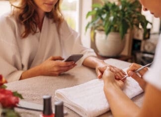 Woman using mobile phone during manicure at spa