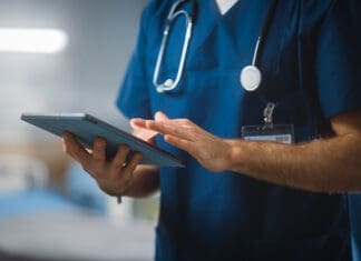 Hospital Ward: Unrecognizable Head Nurse, Doctor, Surgeon Uses Digital Tablet Computer Health Care Vitals Monitoring Computer Machine. Modern Clinic with Advanced Equipment and Professional Working