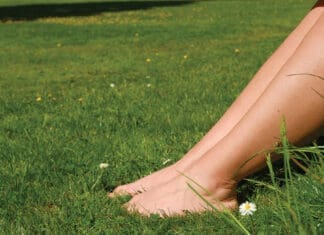 Women's feet on a green lawn in the park. Relaxation, Rest. Grounding. Woman resting on lawn