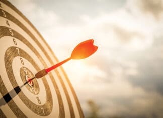 Close up shot red darts arrows in the target of dartboard center on dark blue sky background. Business target or goal success and winner concept.