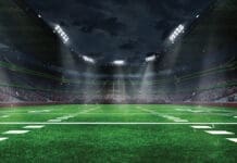 American football arena with yellow goal post, grass field and blurred fans at playground view. 3D render. Flashlights