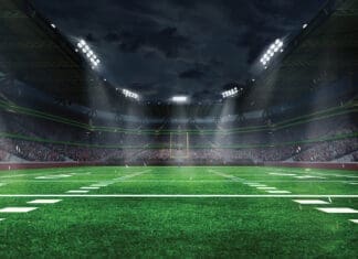American football arena with yellow goal post, grass field and blurred fans at playground view. 3D render. Flashlights