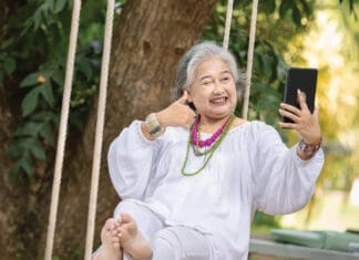Elderly Woman Relaxing on a Swing While Using a Tablet in a Serene Outdoor Setting, Surrounded by Lush Greenery and Natural Beauty