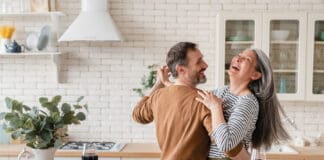 Happy cheerful middle-aged mature couple family parents dancing together in the kitchen, preparing cooking food meal for romantic dinner, spending time together. Active seniors